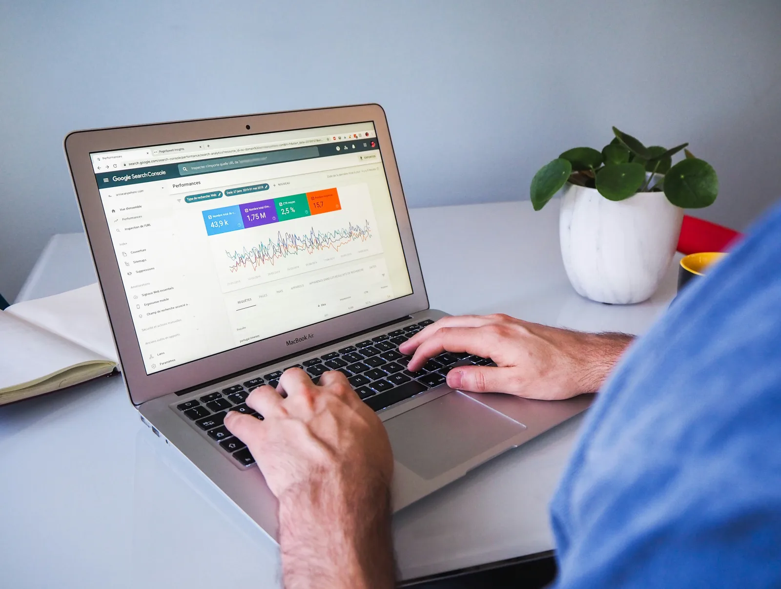 Person reviewing search-performance charts on a laptop beside a notebook and potted plant.