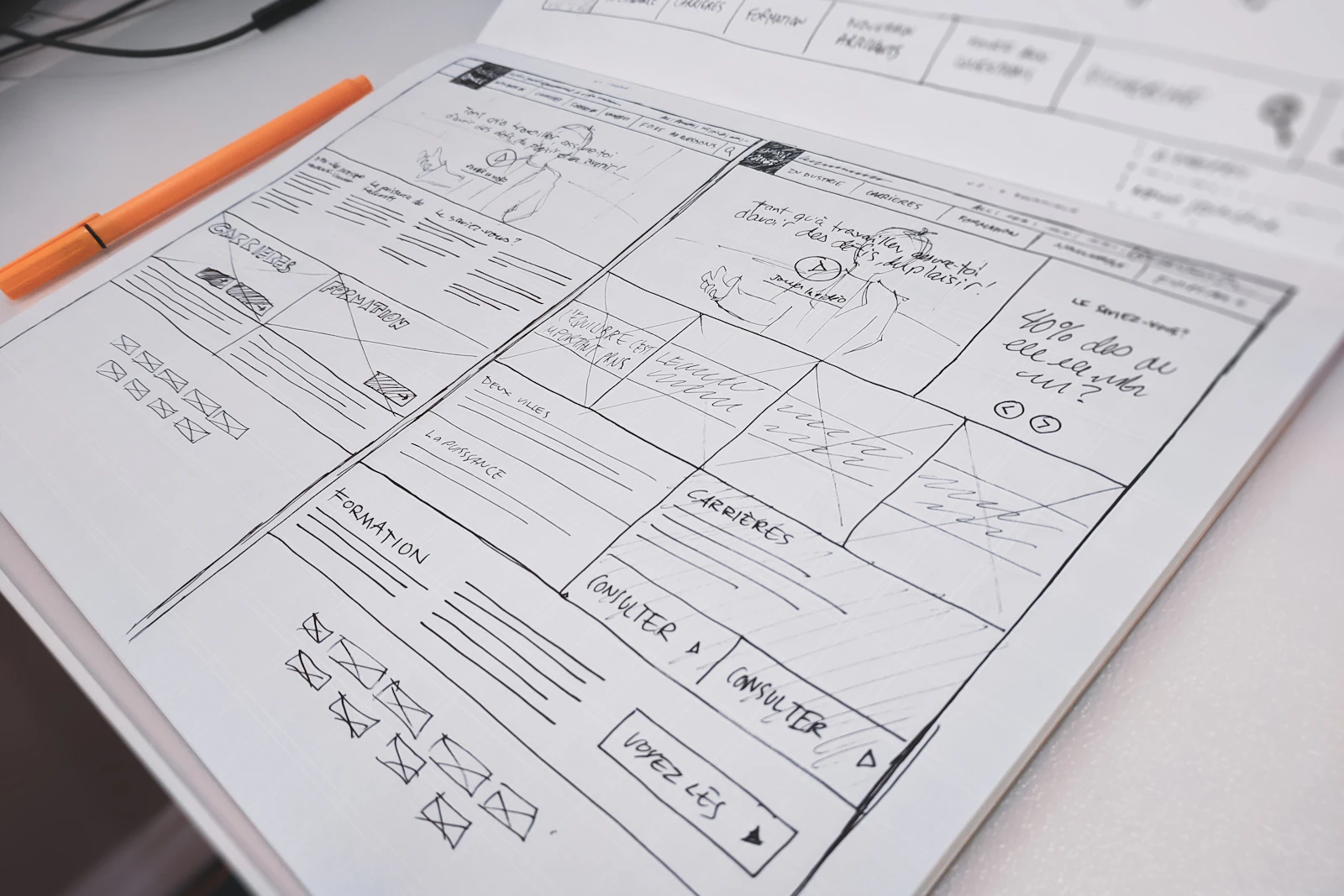 Hand-drawn website layouts on paper beside an orange pen.