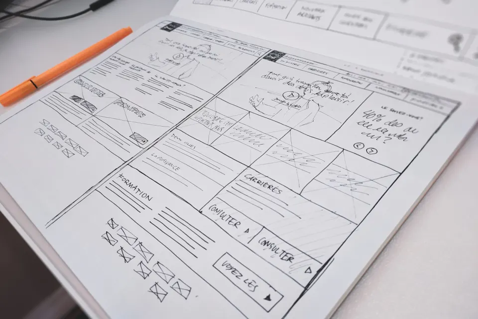 Hand-drawn website layouts on paper beside an orange pen.
